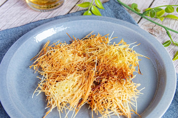 皿に盛られた細いパスタの揚げ物。テーブルにグリーンの装飾と飲み物が添えられている。