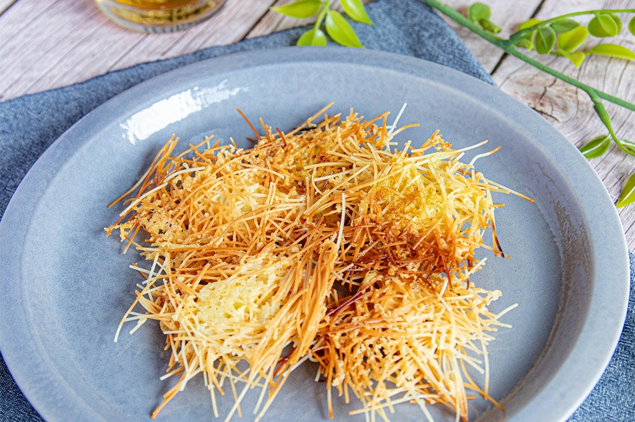 皿に盛られた細いパスタの揚げ物。テーブルにグリーンの装飾と飲み物が添えられている。