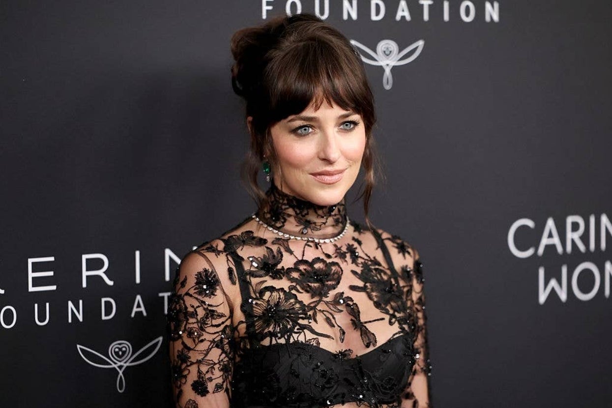 Person in a sheer floral lace dress poses at an event, against a backdrop with text from a foundation
