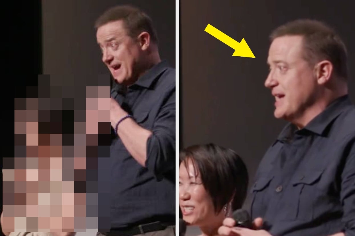 Man in a dark shirt speaking into a microphone on stage, with a blurred individual beside him and a yellow arrow pointing toward him