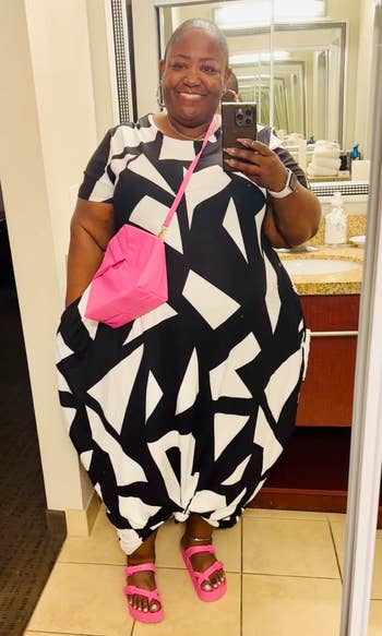 Person successful a achromatic and achromatic geometric formal with a pinkish crossbody container and sandals, taking a reflector selfie successful a bathroom