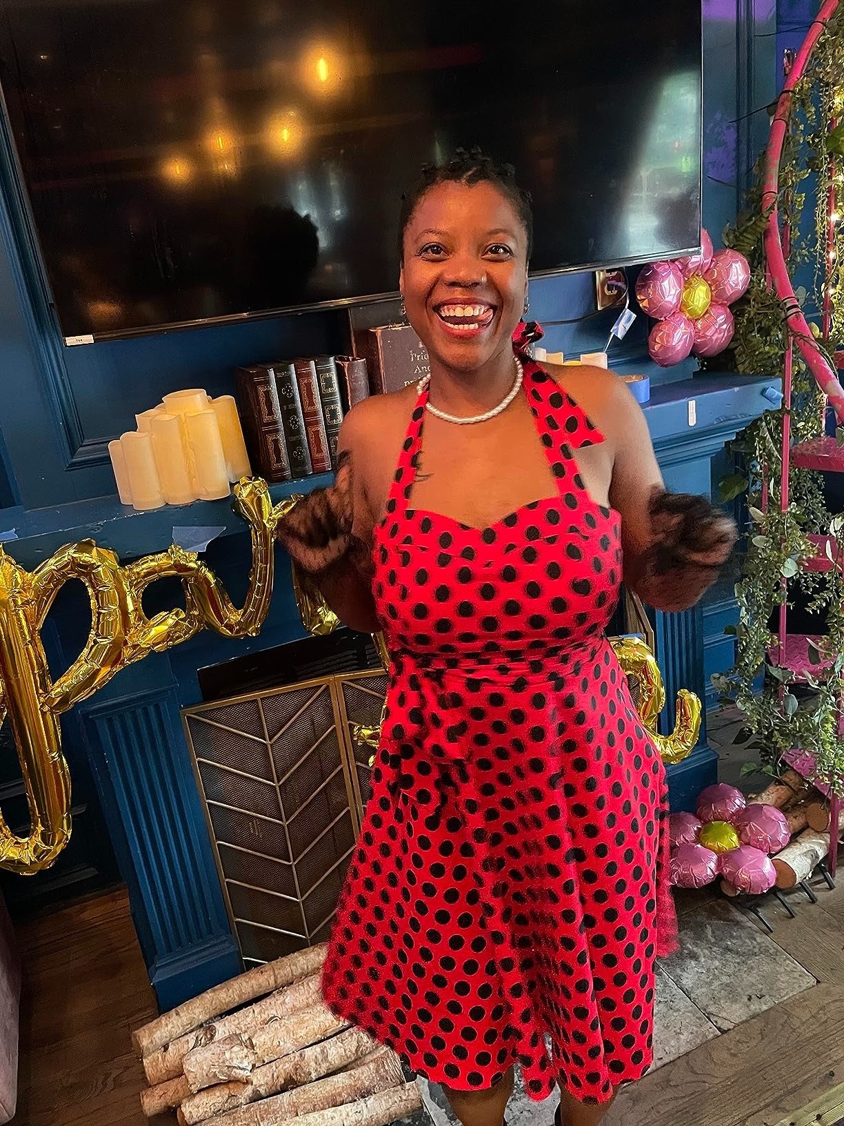 Person smiling, wearing a polka dot formal  with halter neckline, stands amidst decorative candles and balloons successful  a cozy country   setting