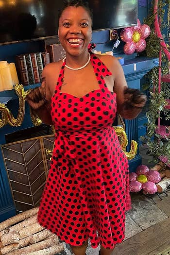 Person smiling, wearing a polka dot formal with halter neckline, stands amidst decorative candles and balloons successful a cozy country setting