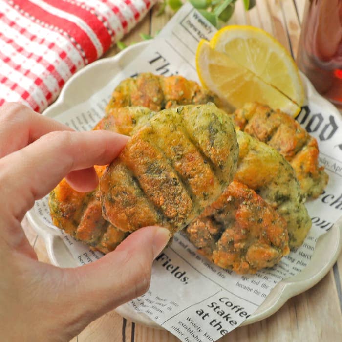 手で持たれたポテト料理が新聞の上の皿に置かれている。隣にレモンスライスが添えられている。