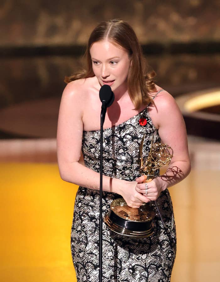 Hannah Einbinder successful patterned one-shoulder gown holds an award, speaking astatine a microphone connected stage
