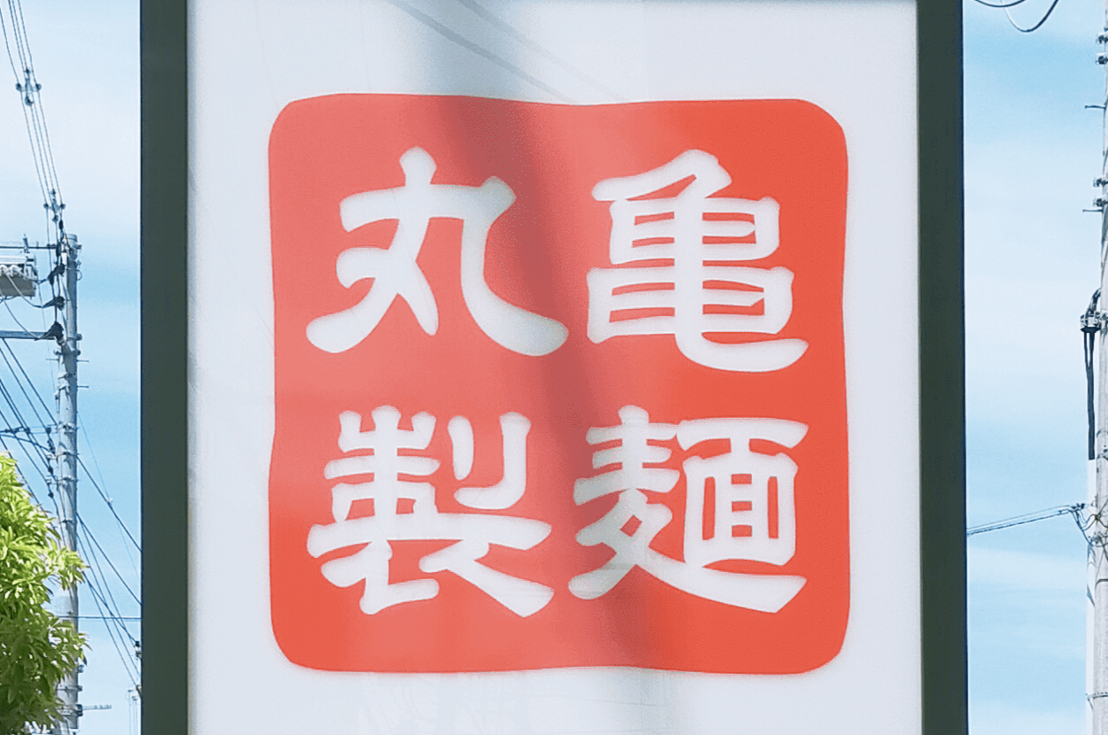 丸亀製麺の看板。背景に電線と青空があります。