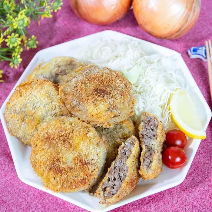 キャベツ、レモン、トマトが添えられた盛り付けられたメンチカツのプレート。テーブルにタンポポと玉ねぎがある。