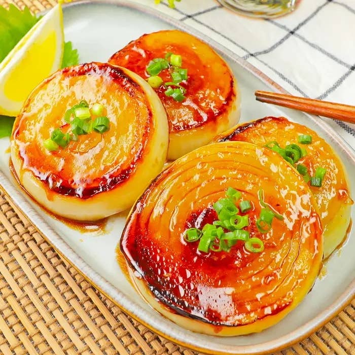 照り焼き風の玉ねぎステーキが皿に盛られ、刻みネギとレモンが添えられている料理の写真。