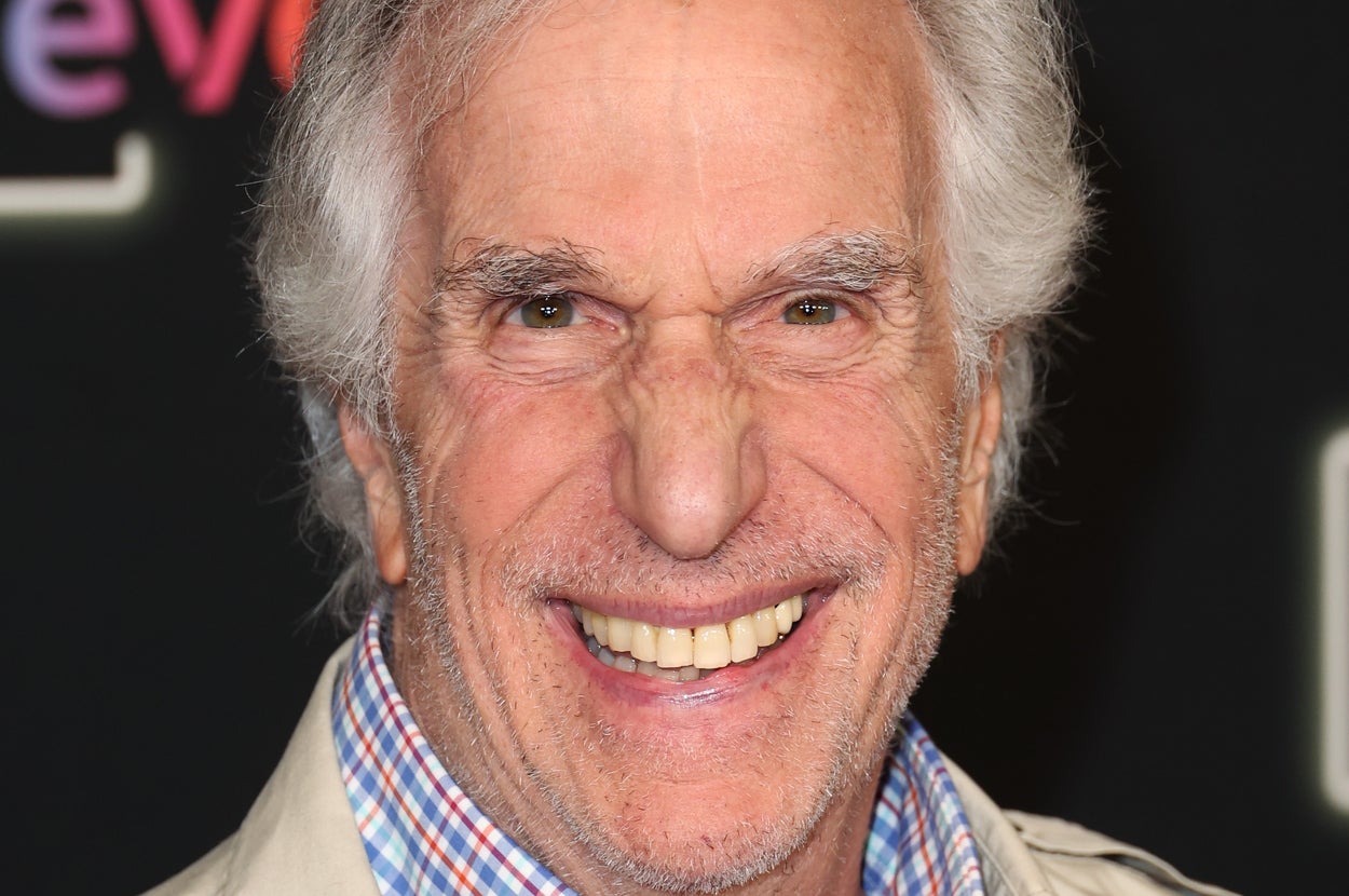Smiling individual in a plaid shirt and light jacket at a formal event