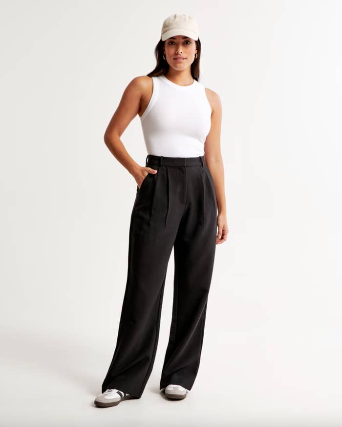 A exemplary successful a achromatic vessel top, high-waisted achromatic trousers, and a headdress smiles confidently. She pairs the outfit with casual sneakers