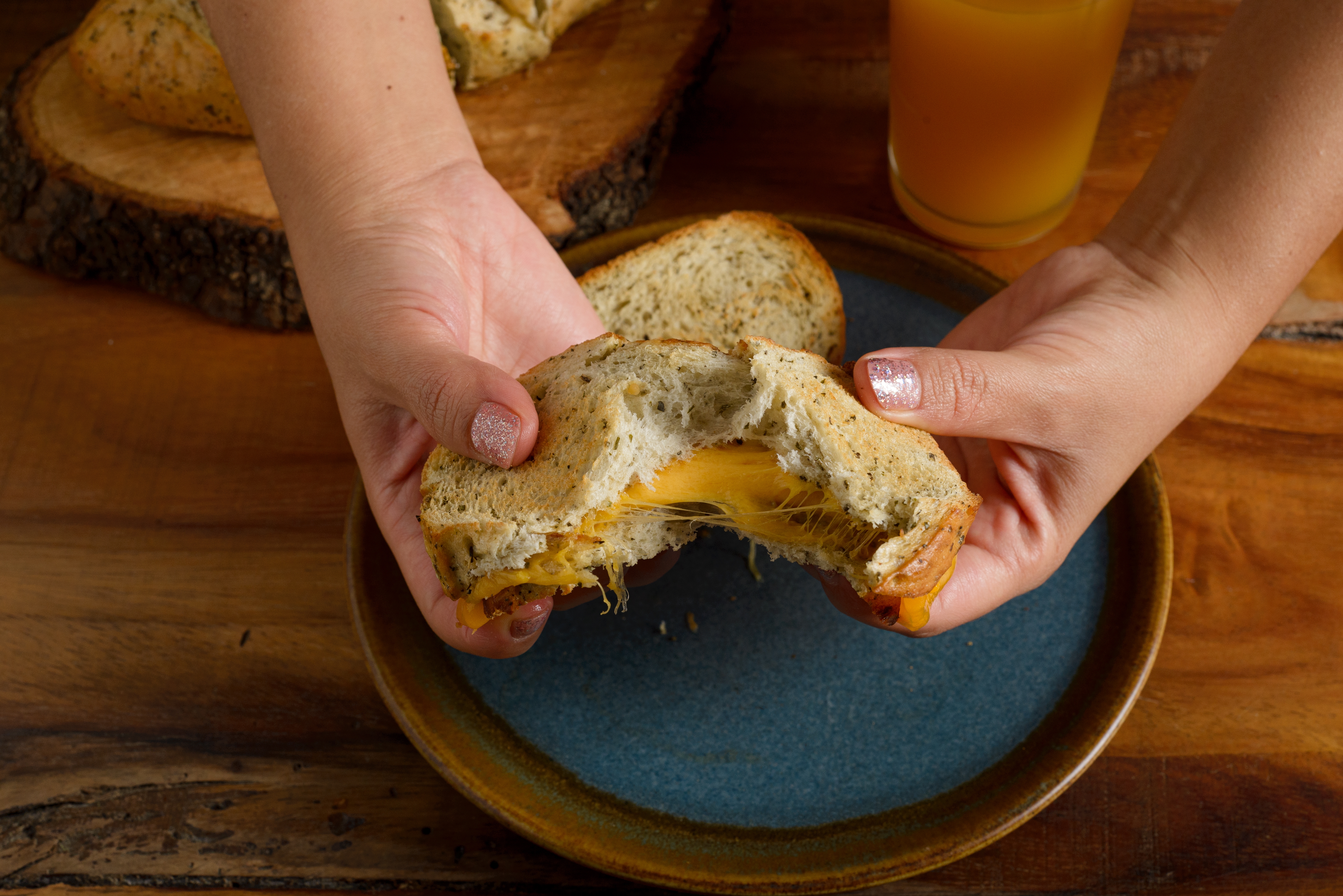 Hender bryter fra hverandre en grillet ostesmørbrød på en tallerken, med juice i bakgrunnen