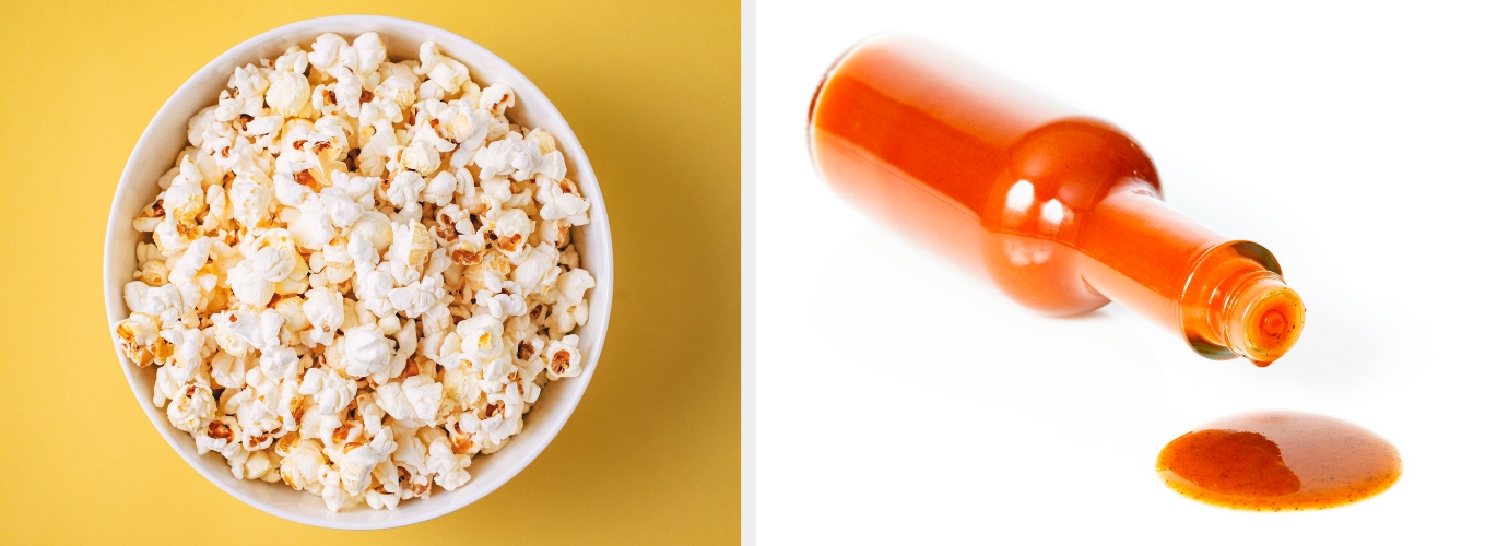 Bowl of popcorn next to a bottle of spicy hot sauce with a spill on a white surface