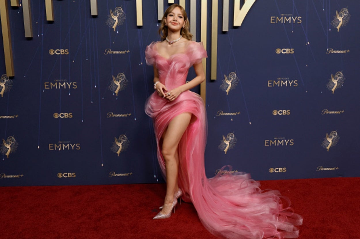 Person in an elegant, flowing gown with sheer details poses on a red carpet at a formal event
