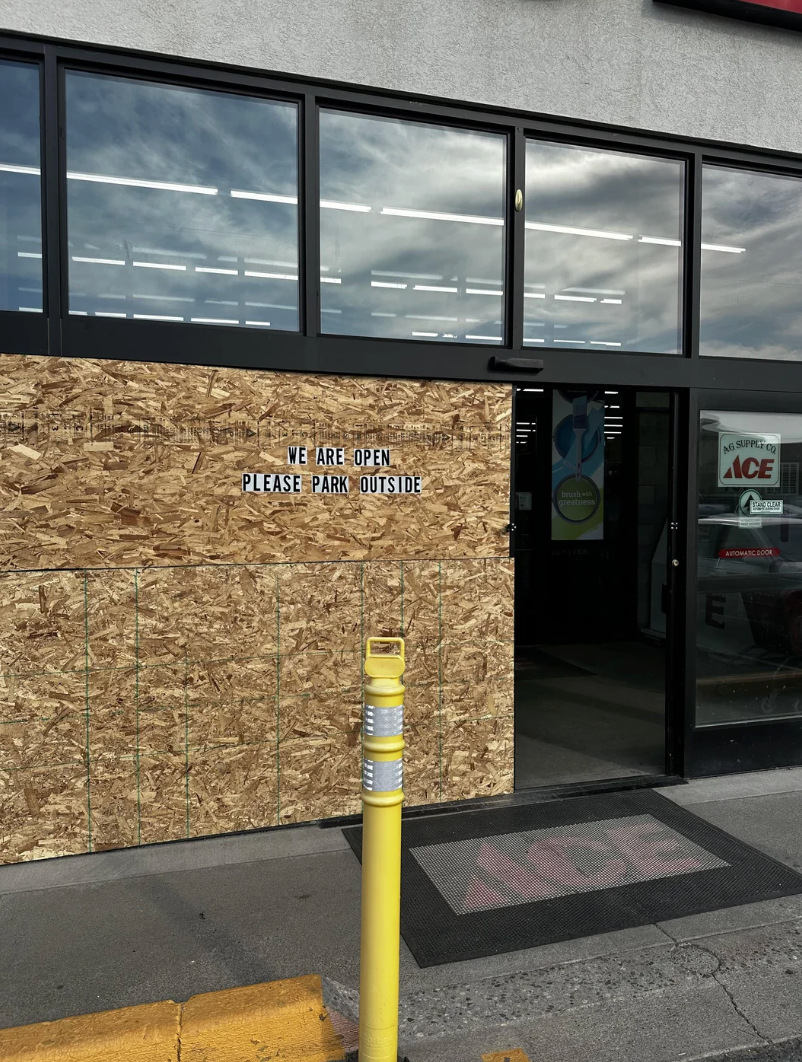 Store entranceway  with boarded-up windows, motion   says "We are open. Please parkland  outside."