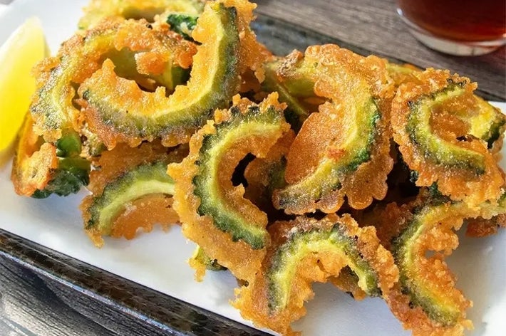 お皿にゴーヤの天ぷらが盛られている。隣にレモンと飲み物も配置され、美味しそうに見える。