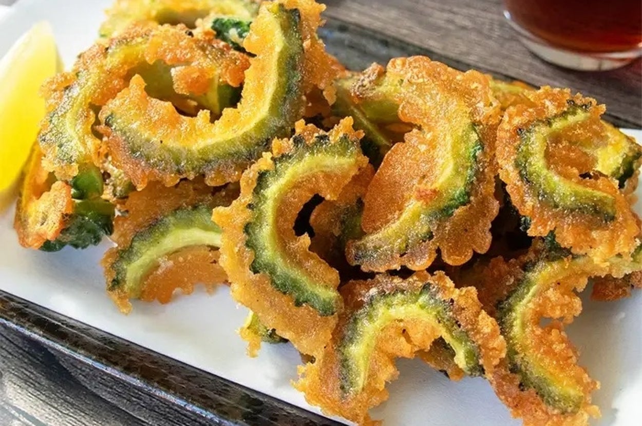 お皿にゴーヤの天ぷらが盛られている。隣にレモンと飲み物も配置され、美味しそうに見える。