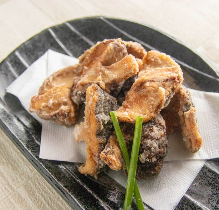 しいたけの唐揚げ。皿に盛られた揚げたキノコの料理。紙ナプキンが下に敷かれ、数本のチャイブが添えられています。