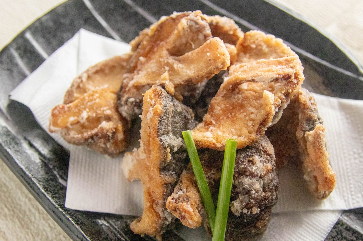 黒い皿に盛られた揚げたキノコ料理。上に緑のネギが添えられている。