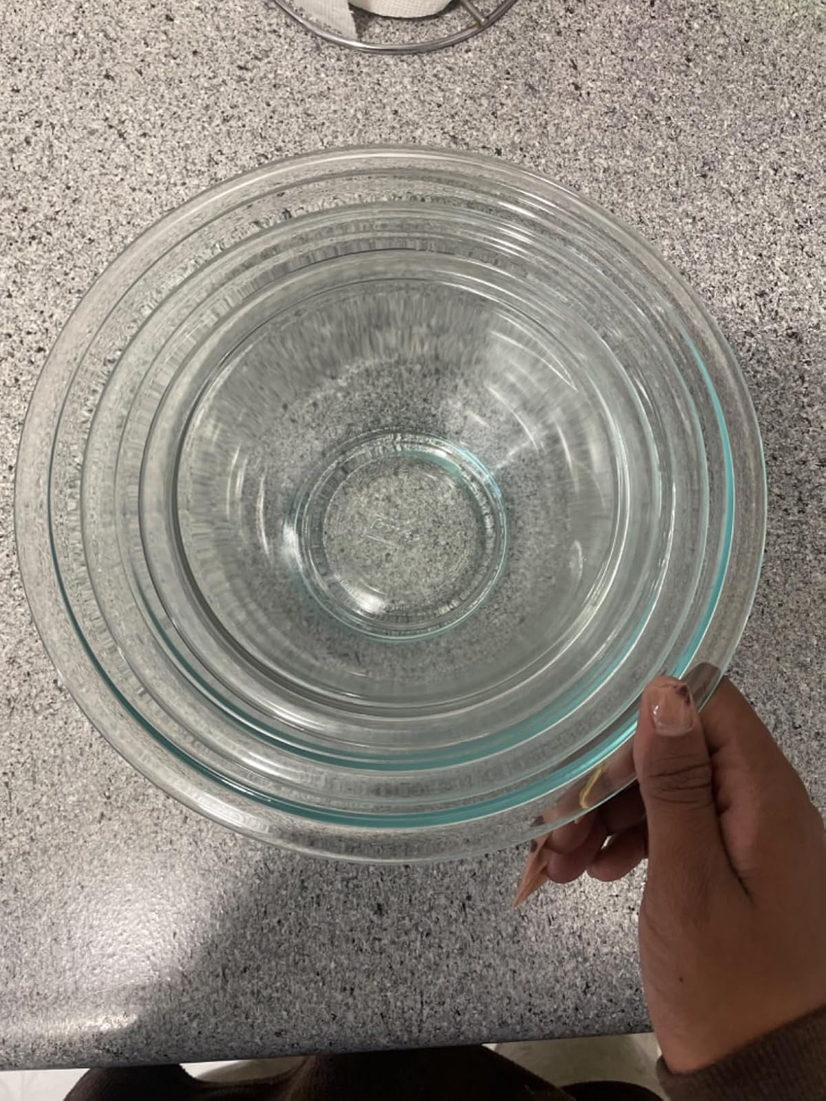 Person holding stacked glass mixing bowls on a countertop