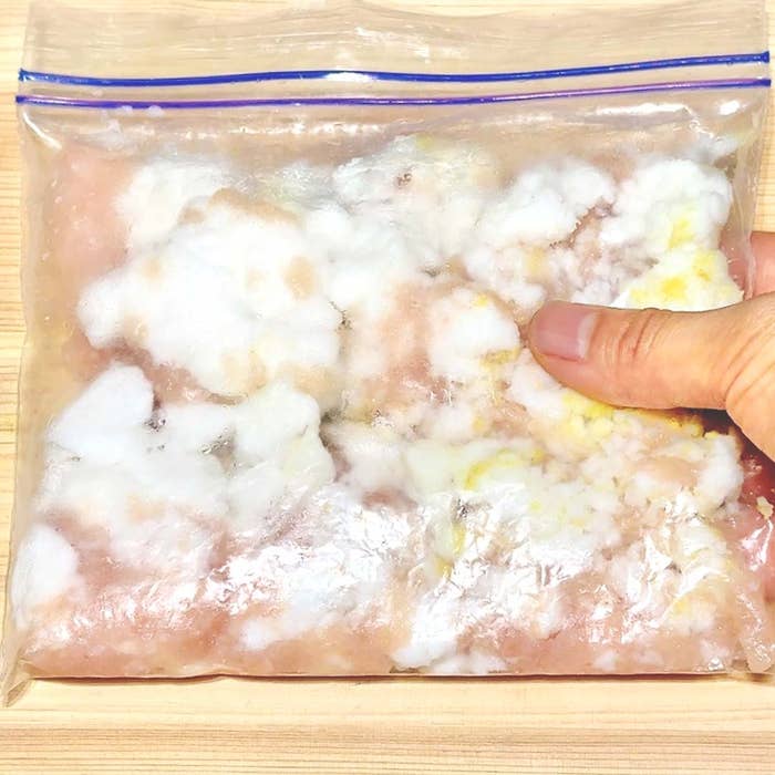 ビニール袋に入った白いカビの生えた食品が手で押されています。