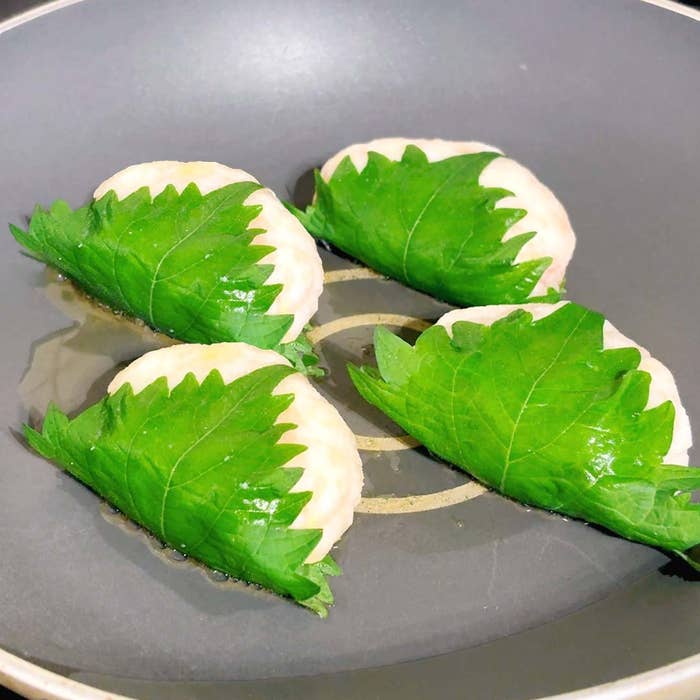 フライパンでシソの葉で包まれた餃子が4つ調理されています。
