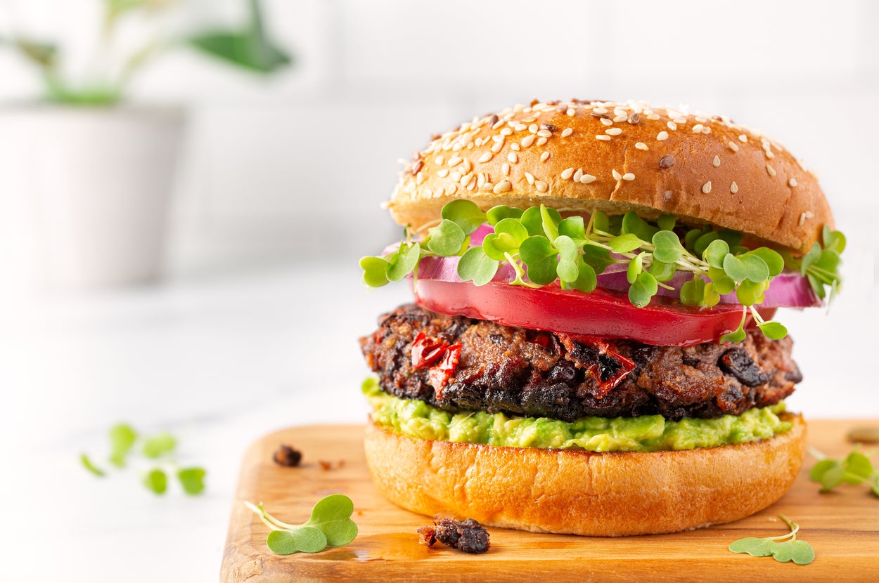 Gourmet vegan burger with a patty, tomato, microgreens, and avocado on a sesame bun, placed on a wooden tray