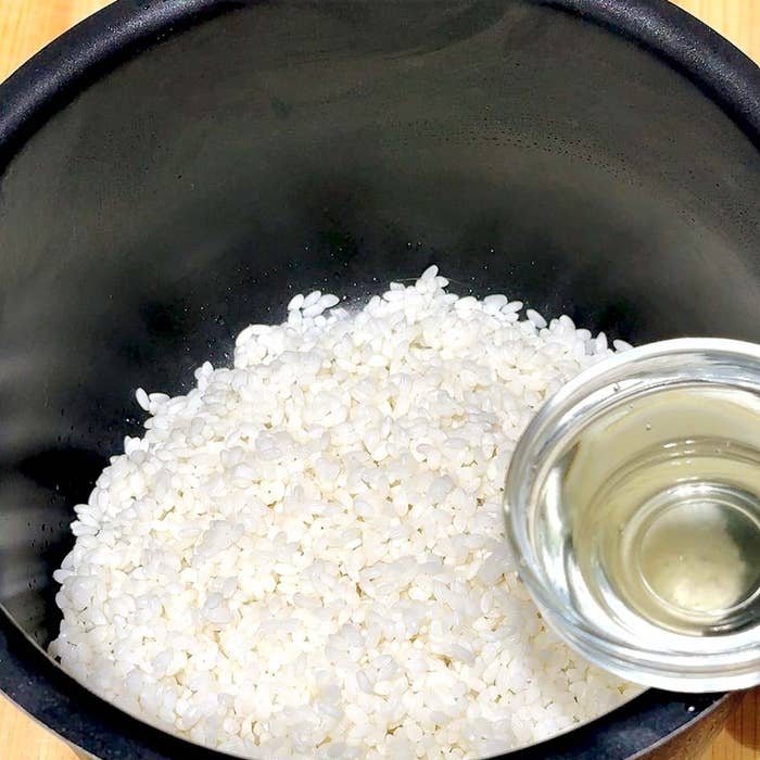 炊飯器に生の米と、水が注がれている透明なカップ。