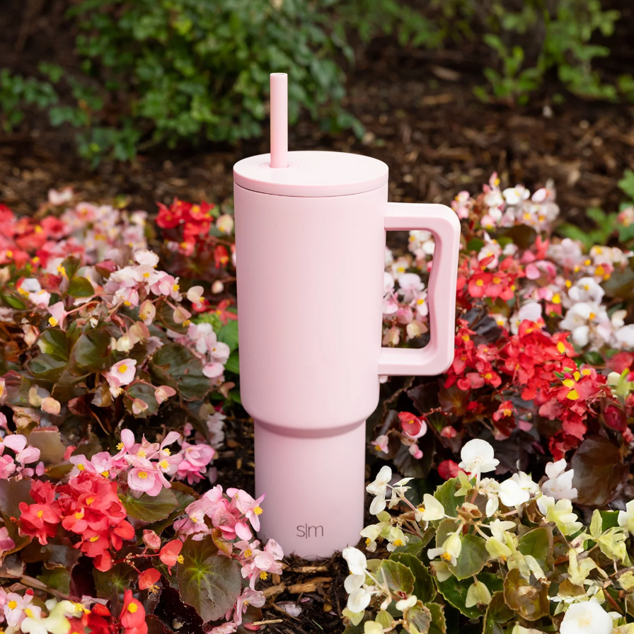 A pinkish  insulated tumbler with a grip  and straw is placed among colorful flowers successful  a plot  setting