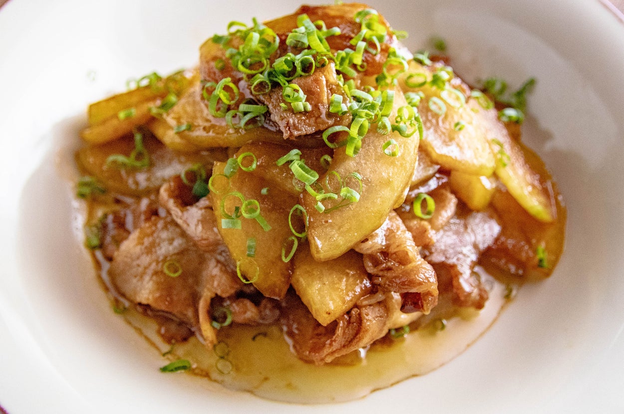 お皿に盛られた豚肉とポテトの炒め物、上に刻んだネギが添えられています。