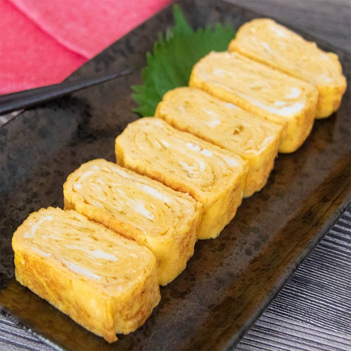 カレー粉が入った卵焼きが黒い皿に6切れ並べられている。背景に大葉と箸が見える。