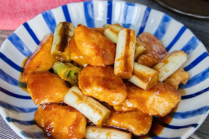 青い縞模様の器に盛られた照り焼きチキンとネギの料理。食欲をそそる見た目です。