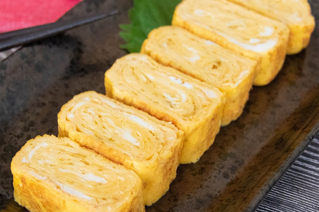 カレー粉が入った卵焼きが黒い皿に6切れ並べられている。背景に大葉と箸が見える。
