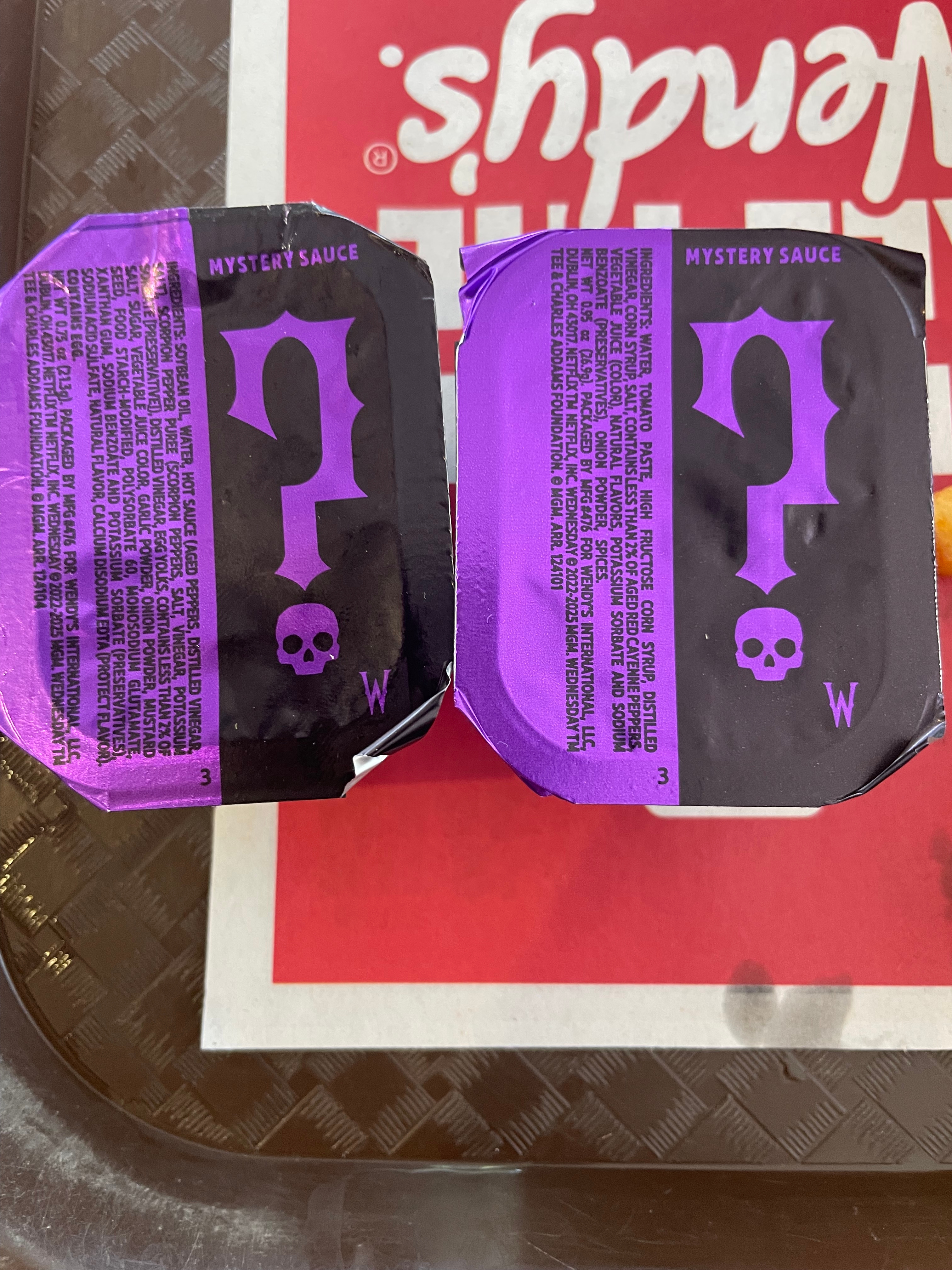 Two containers of "Mystery Sauce" with purple skull designs are placed on a tray branded with "Wendy's."