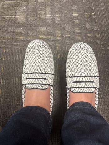 Person wearing achromatic patterned loafers, viewed from above, connected a carpeted floor