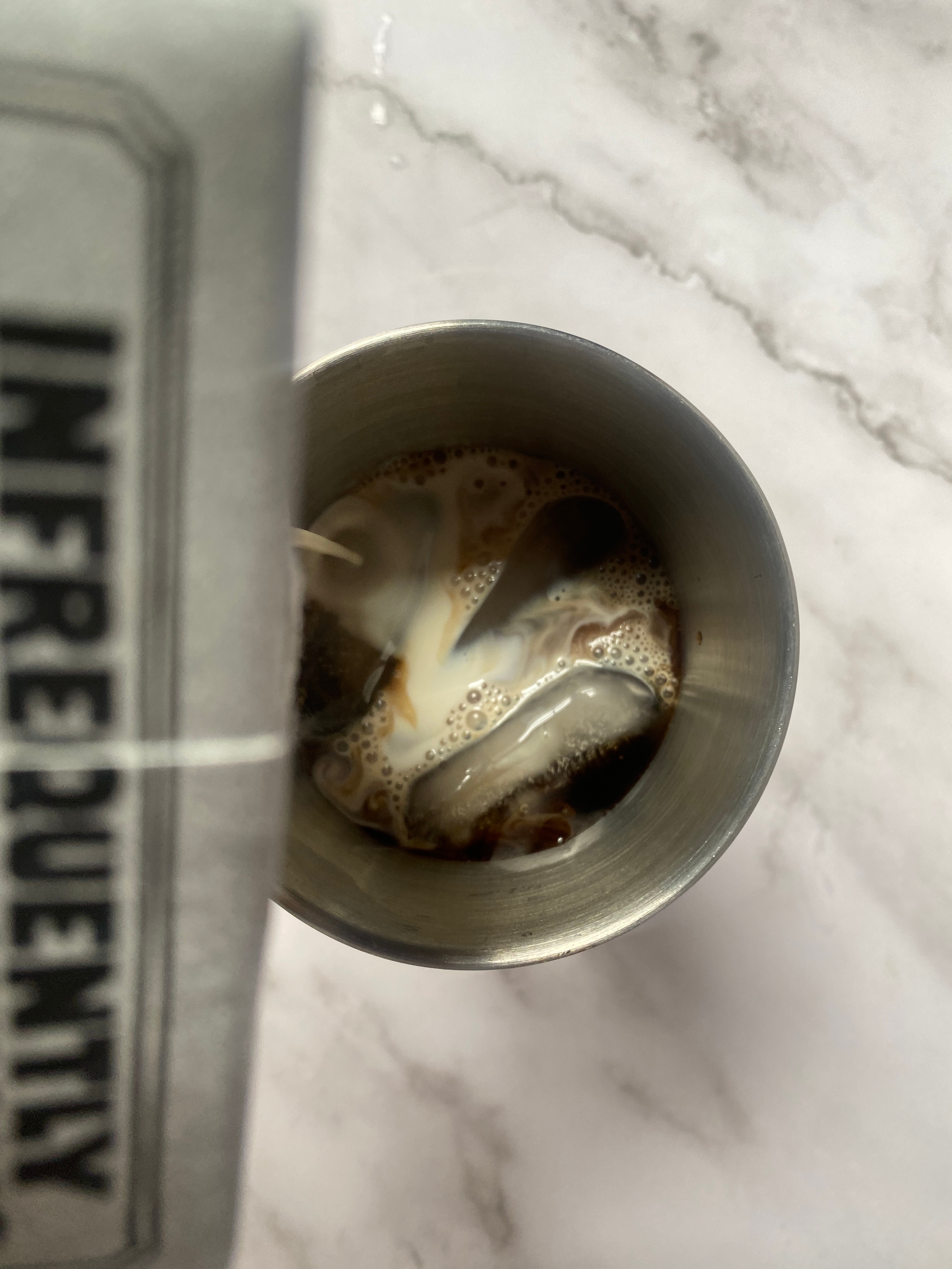 Pouring milk from a carton labeled "INFREQUENTLY" into a cup of coffee on a marble surface