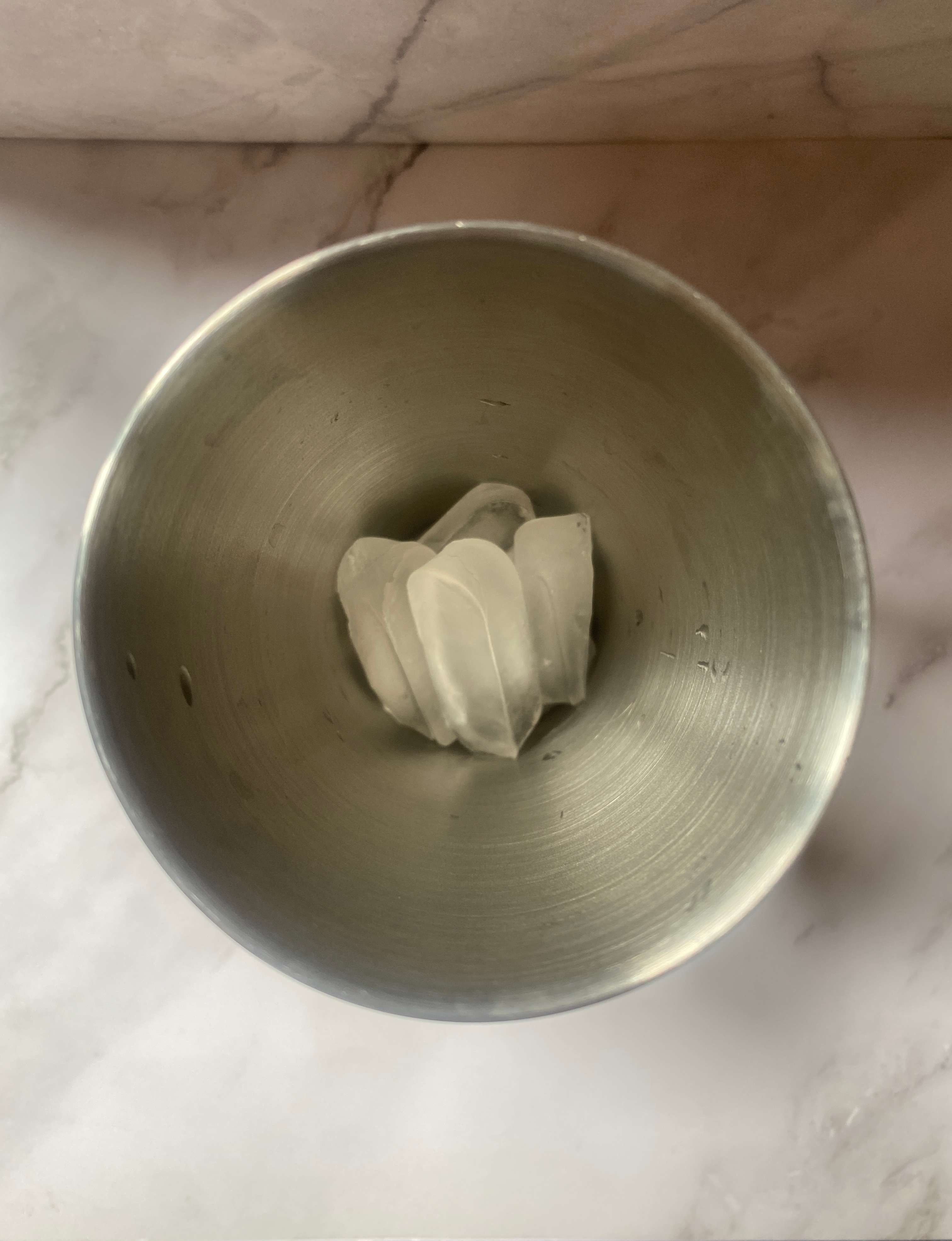Stainless steel cocktail shaker with three ice cubes placed at the center. Marble countertop background