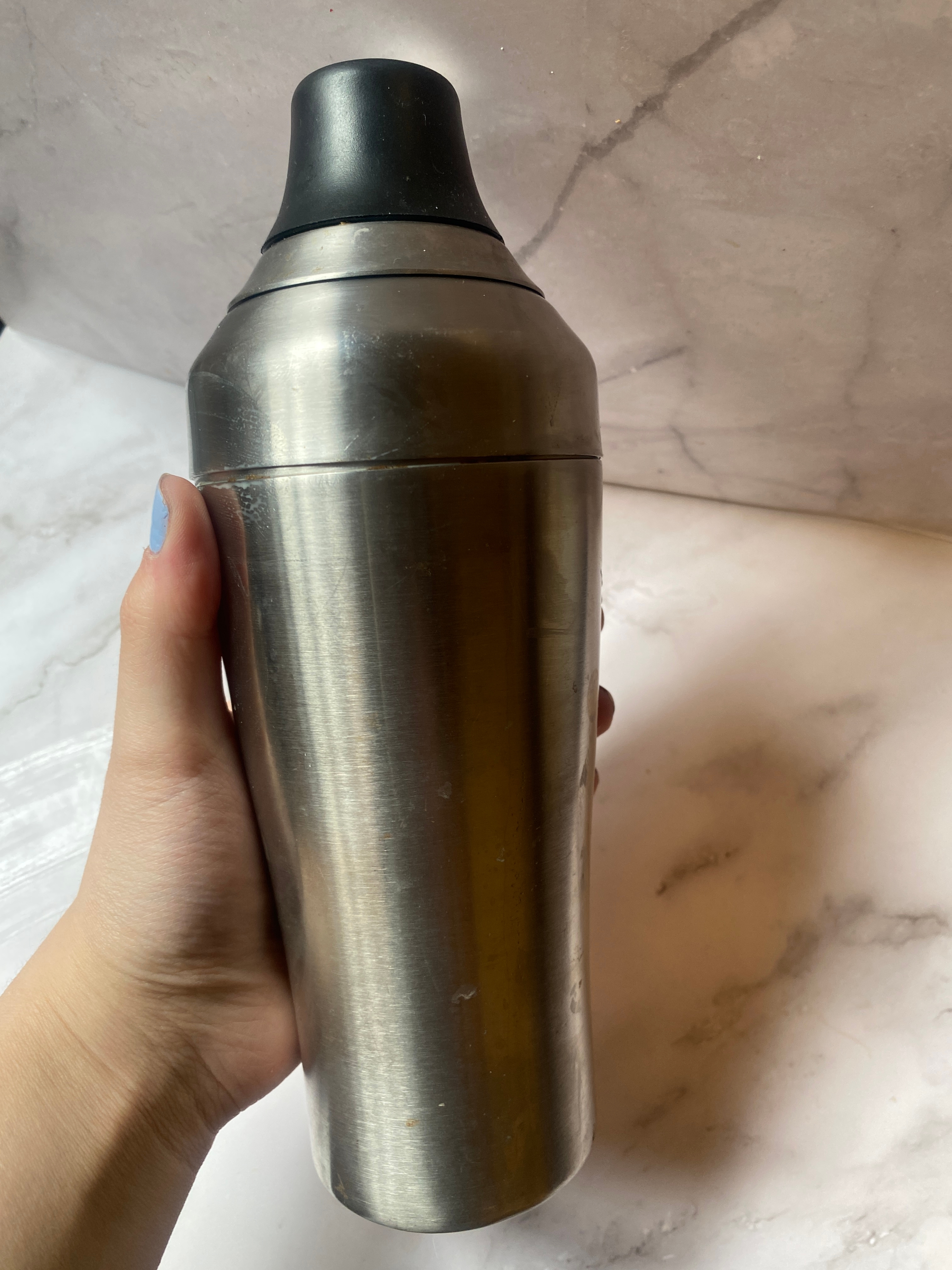 Hand holding a stainless steel cocktail shaker against a marble background