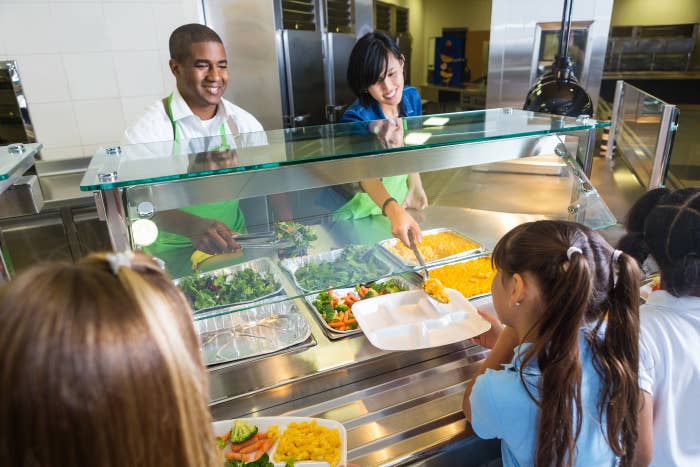 Cafeteria workers service nutrient to children from down the counter