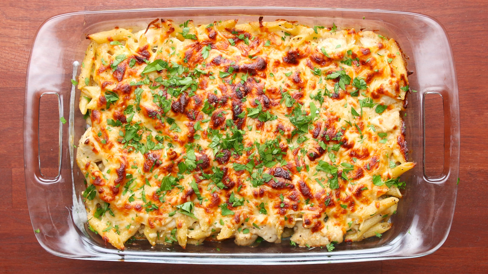 Baked pasta with melted cheese and chopped herbs in a glass dish