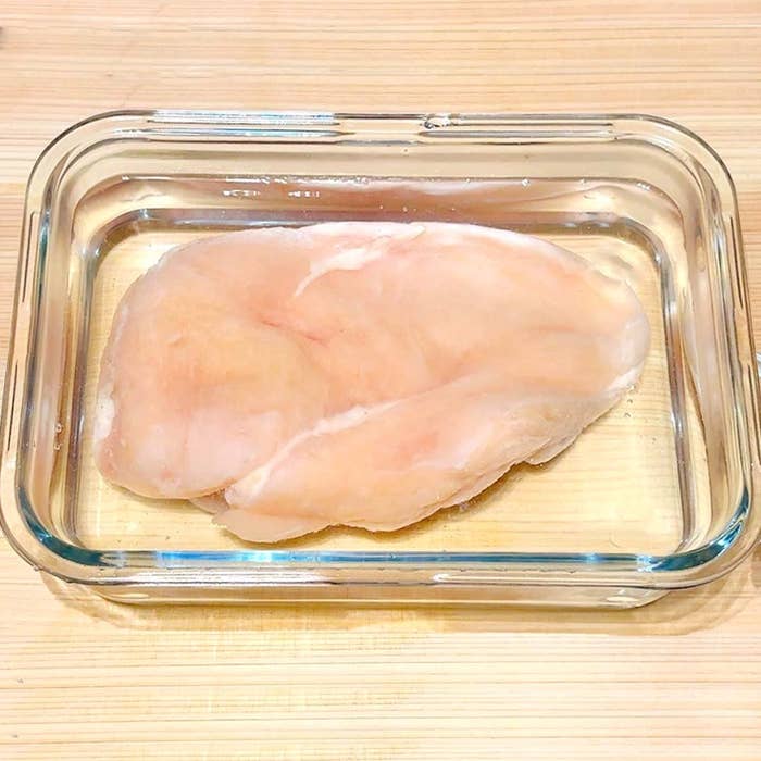 ガラス容器に入った生の鶏むね肉一枚が木製の台の上に置かれている。