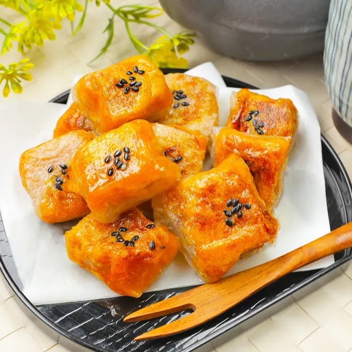 黒ゴマがトッピングされた角形の焼き菓子が皿に乗っている。隣に木のフォークが置かれている。