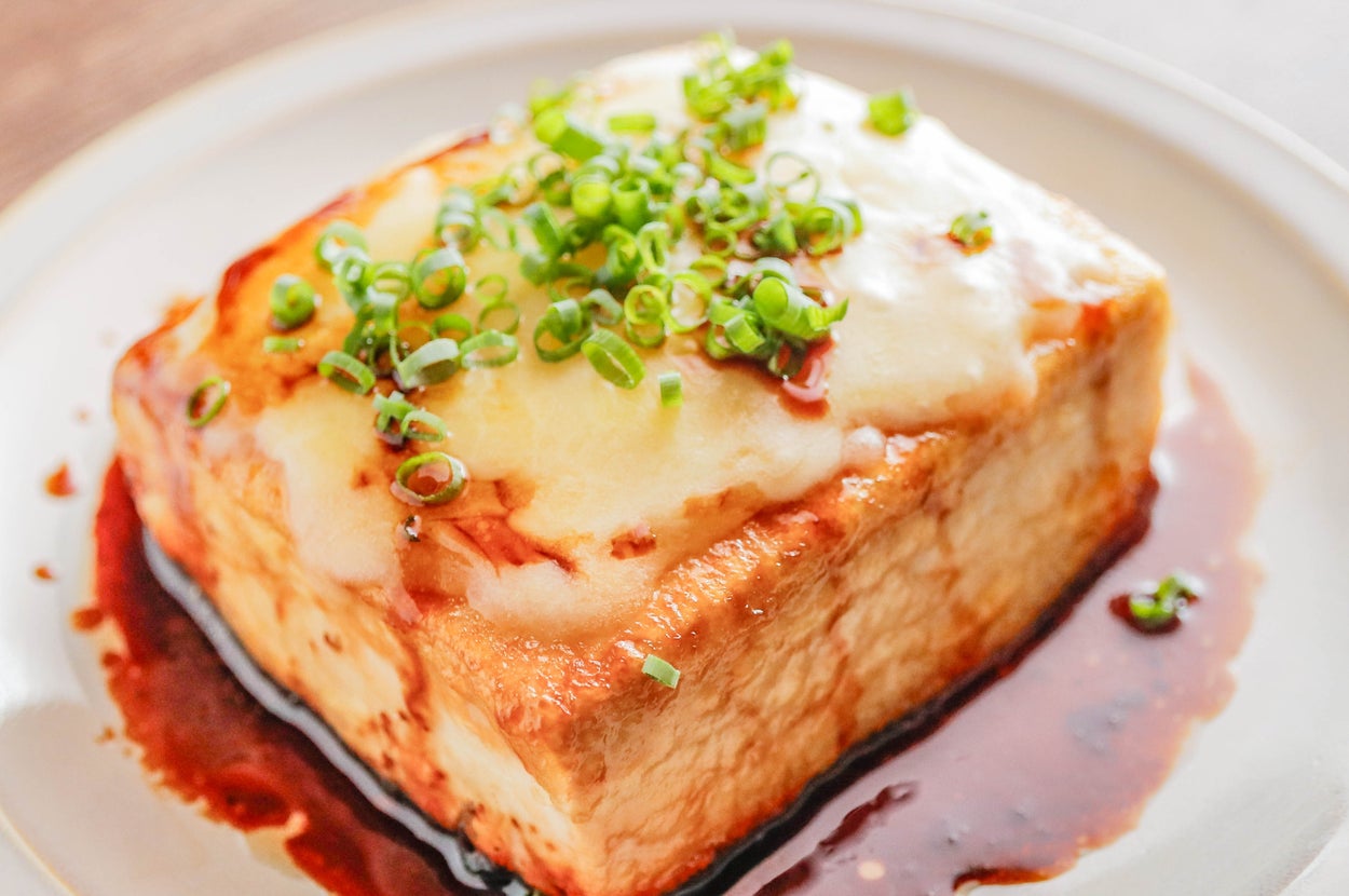 皿に盛られた厚切り豆腐、ソースがかかり、刻みネギと溶けたチーズがトッピングされています。