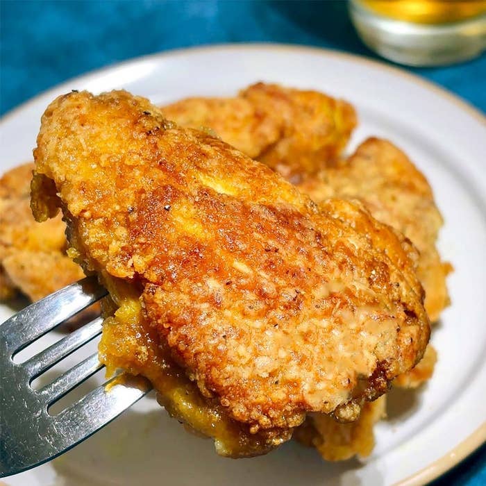フォークに刺したフライドチキンのアップ。奥には他のチキンと飲み物が見える。