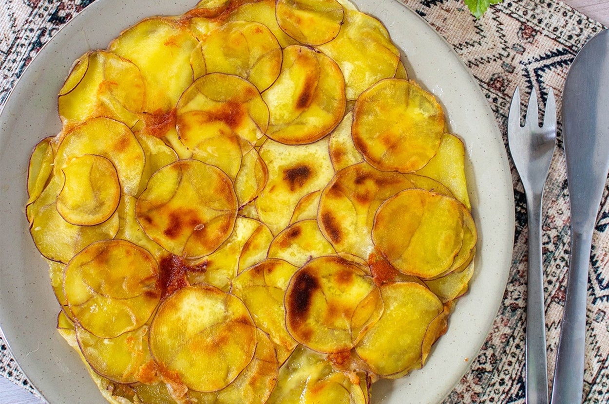 薄切りポテトが重なり合った焼き料理が皿に盛られている。飾りの葉がそばに置かれている。