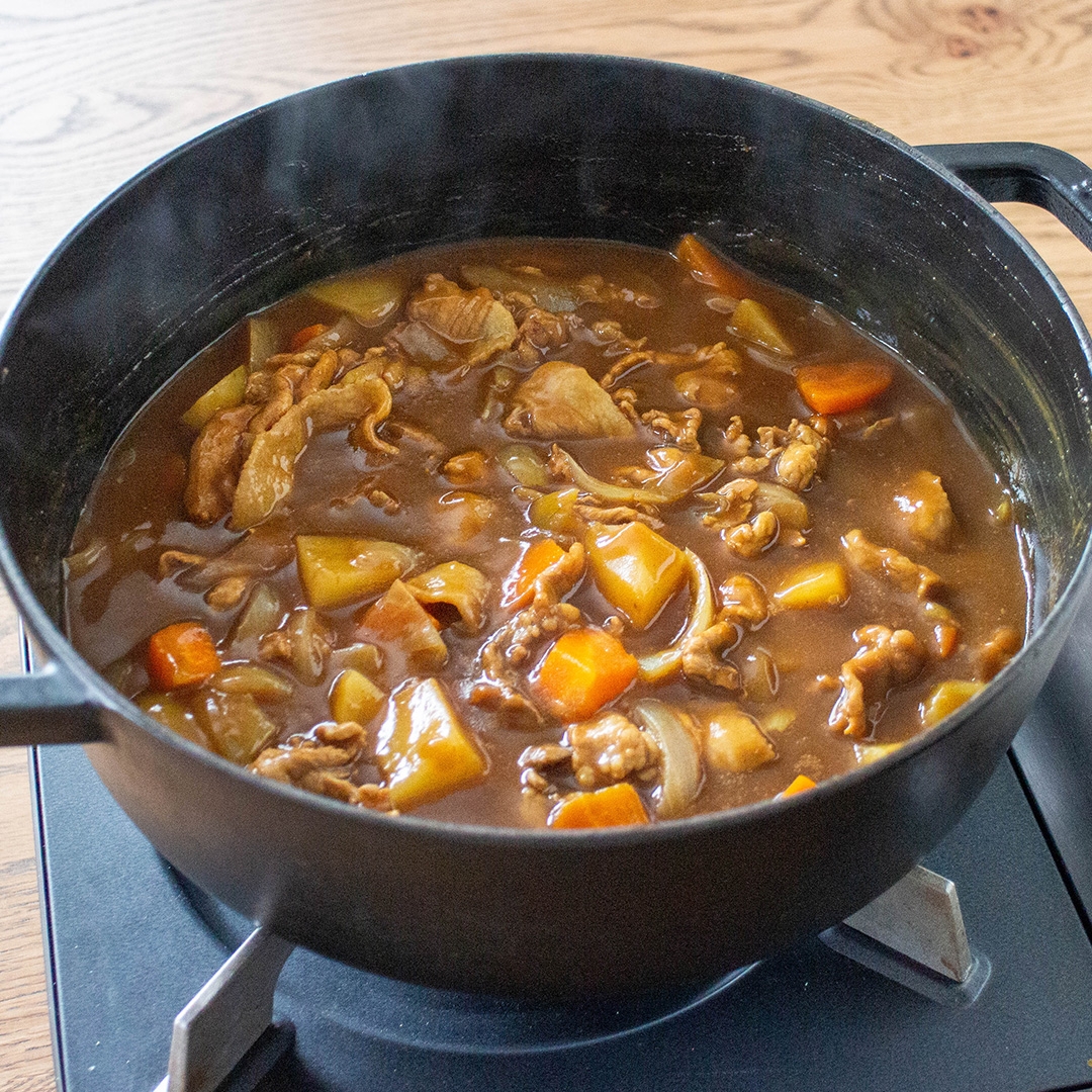 鍋で煮込まれた具沢山のカレー。じゃがいも、にんじん、肉が見える。