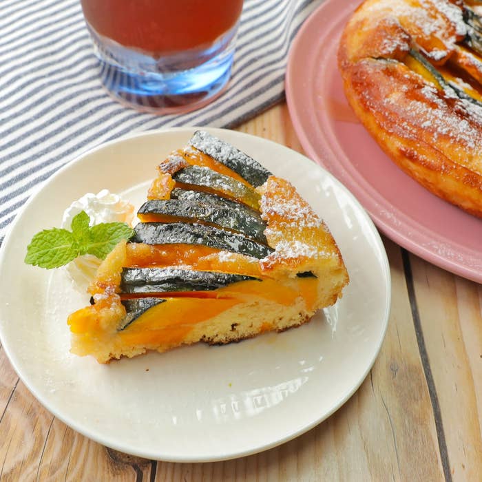 プレートに盛られたカボチャのタルト、ホイップクリームとミントが添えられています。背景に飲み物とタルトの全体像が見えます。
