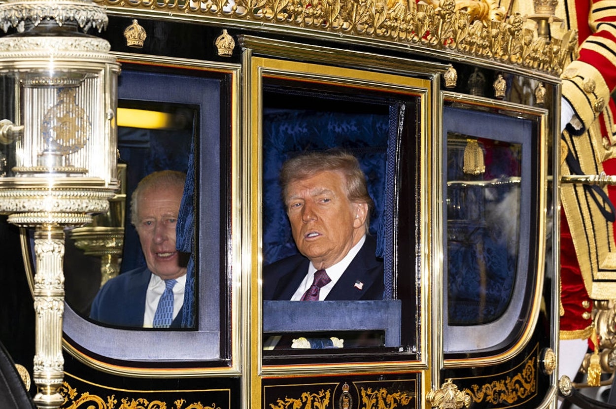Two individuals in formal attire are seated inside a royal carriage, surrounded by ornate decorations