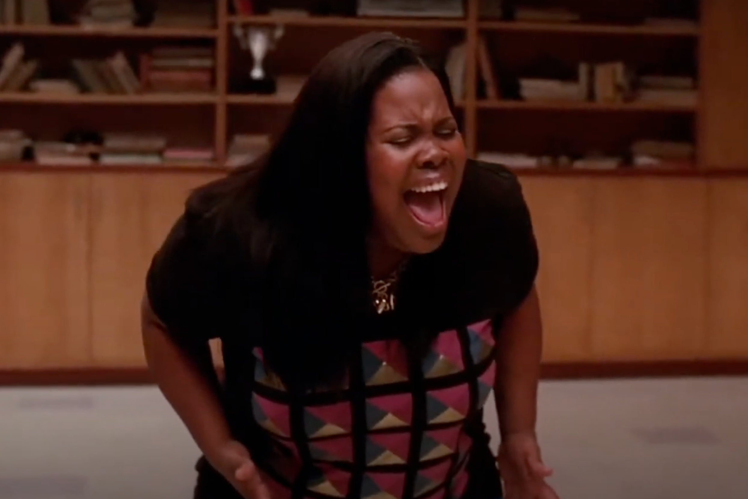 Person passionately singing in a room with bookshelves and wooden cabinets in the background
