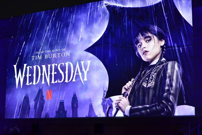 Billboard of Netflix's "Wednesday" series featuring a character in a striped coat holding an umbrella against a gothic backdrop