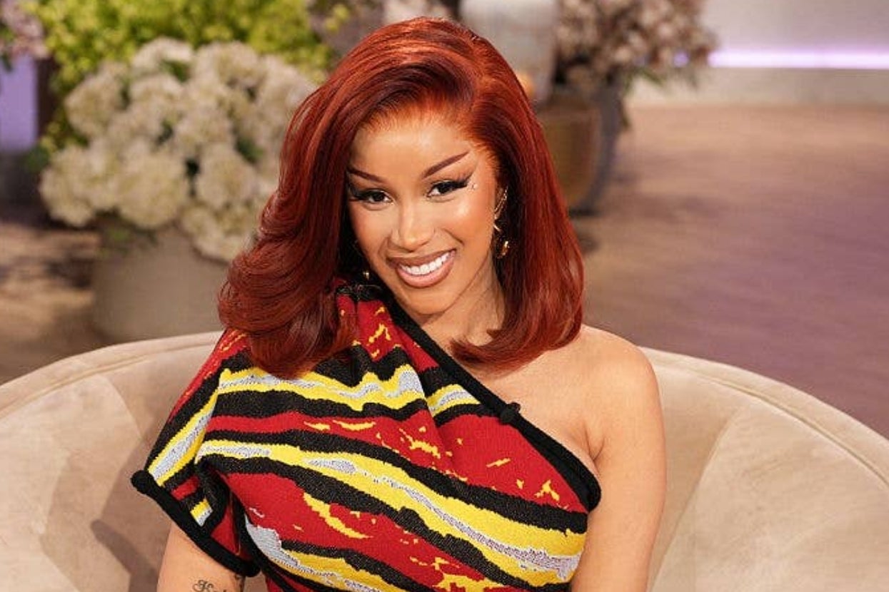 A person wearing an asymmetrical, patterned top smiles while seated, with styled hair falling on one shoulder in a relaxed interview setting